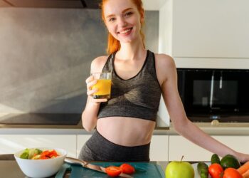 woman standing smiling in kitchen in workout gear drinking juice