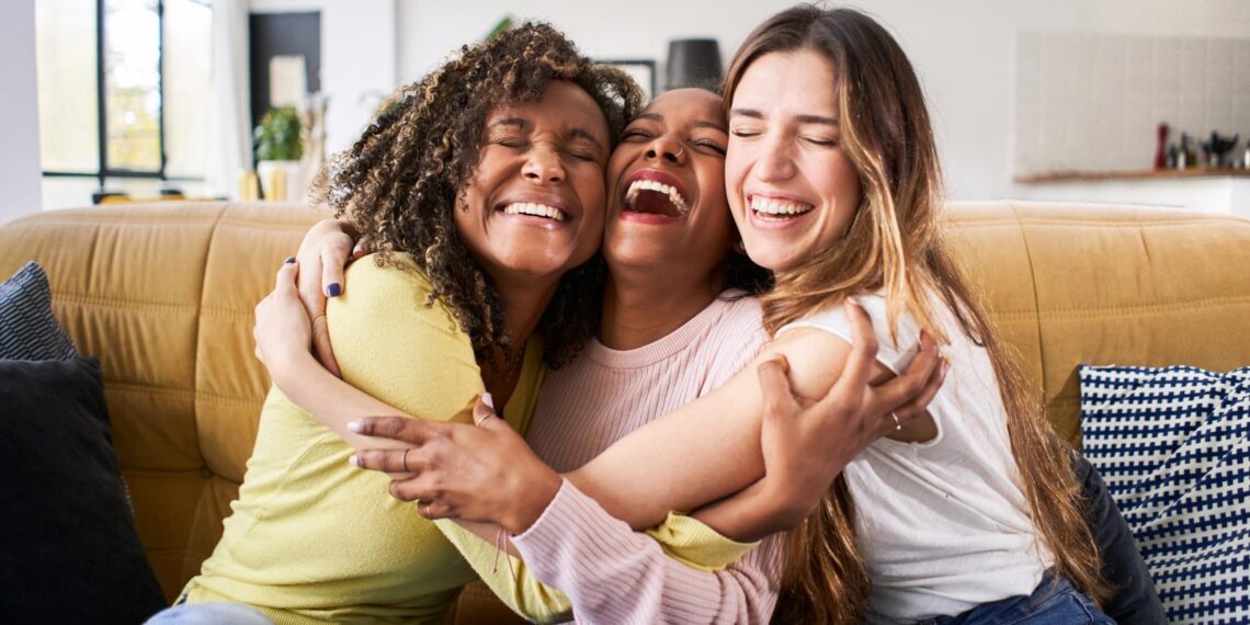 Three women smiling, laughing and hugging each other on a couch