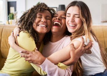 Three women smiling, laughing and hugging each other on a couch