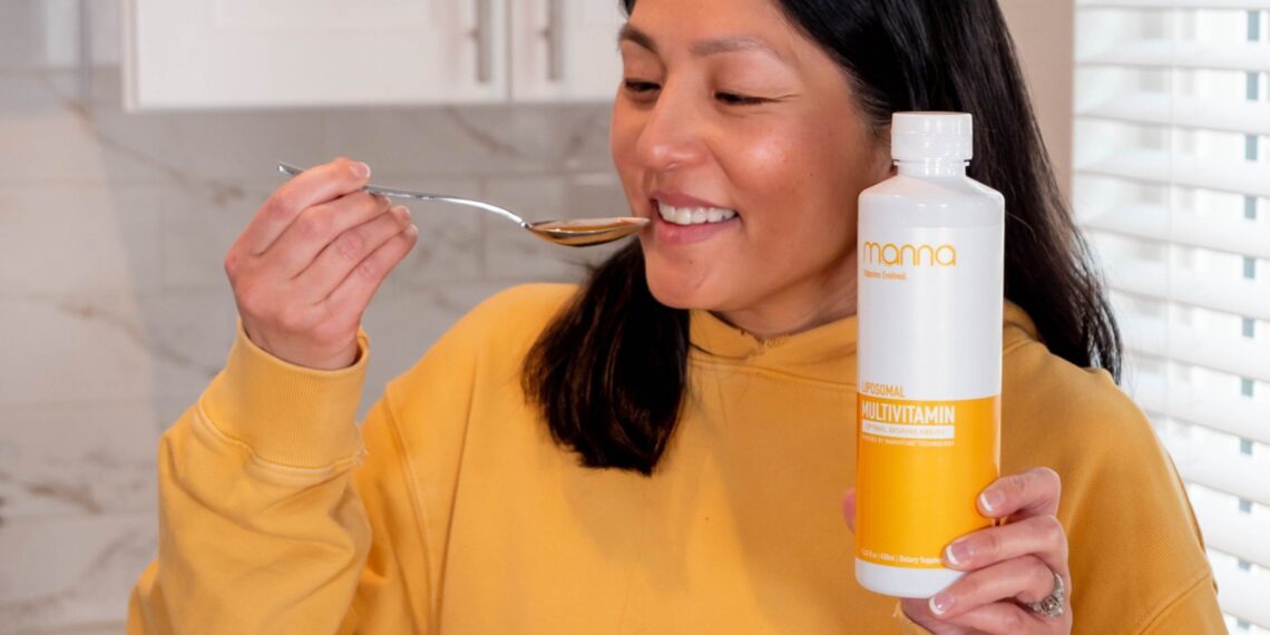 A woman smiling while preparing to take liquid from a spoon, holding a bottle labeled as a multivitamin supplement.