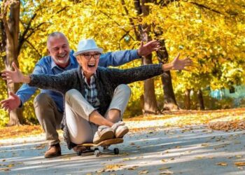 Two joyful seniors having fun on a skateboard in a park during autumn.