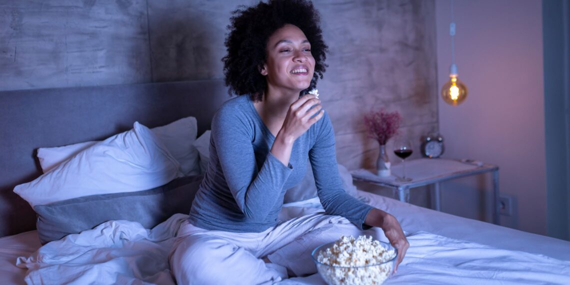 woman snacking on popcorn in bed