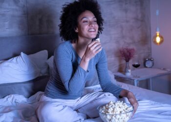 woman snacking on popcorn in bed