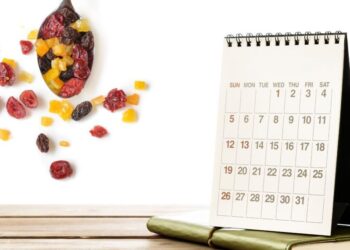 A desk calendar on a wooden surface with scattered dried fruits and a potted plant.