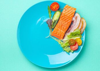 A plate with a raw salmon fillet and fresh vegetables on a turquoise background.