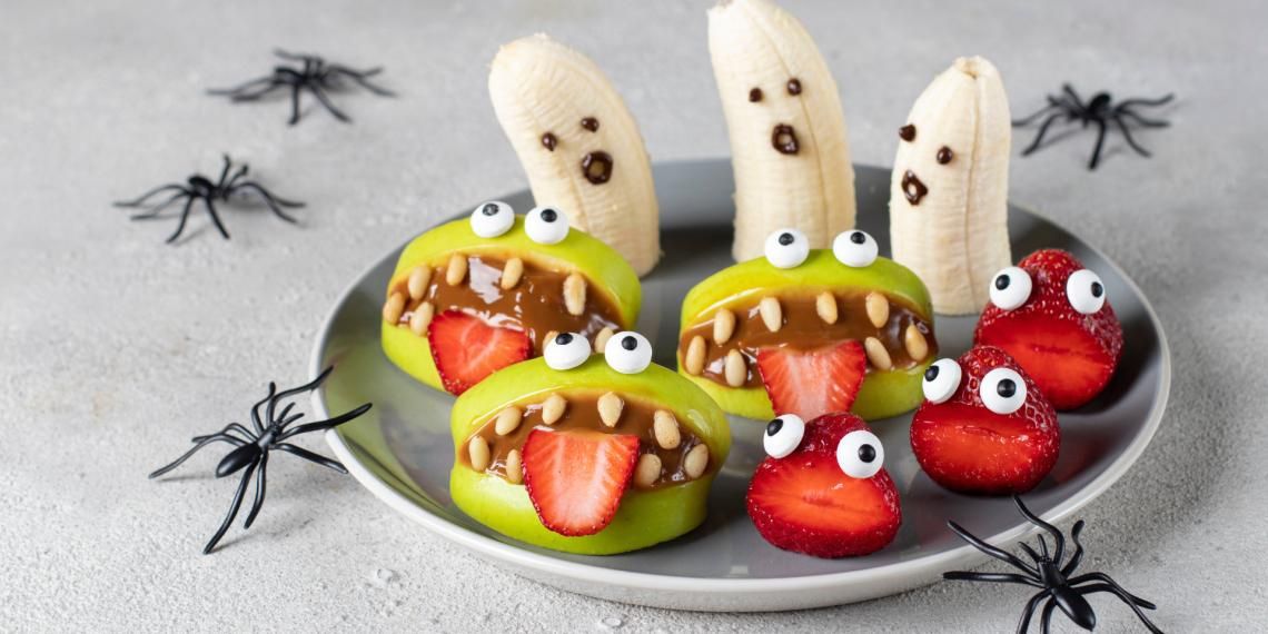 Healthy fruit snacks creatively designed to look like monsters and ghosts for halloween, decorated with candy eyes and displayed on a plate with decorative spiders around.