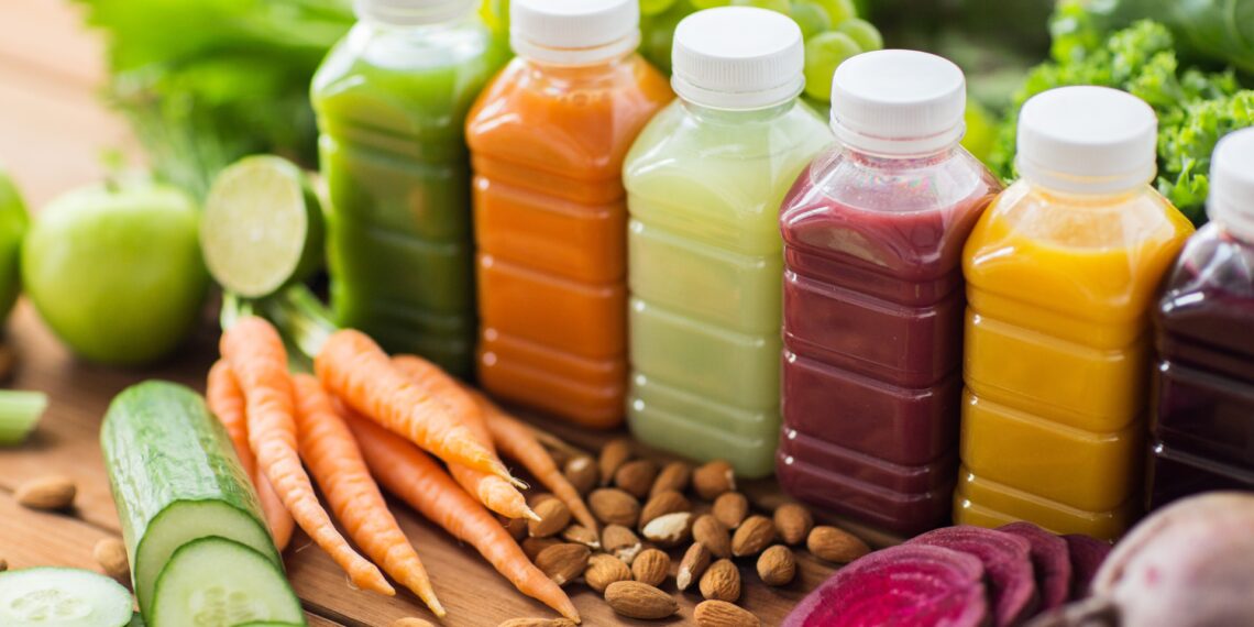 multiple smoothies in bottles with an assortment of fruits and veggies