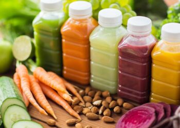 multiple smoothies in bottles with an assortment of fruits and veggies