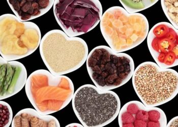 Assorted heart-healthy foods in heart-shaped bowls arranged on a black background.