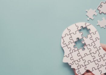 A hand is holding a white puzzle in the shape of a human head with a few missing pieces against a light blue background.