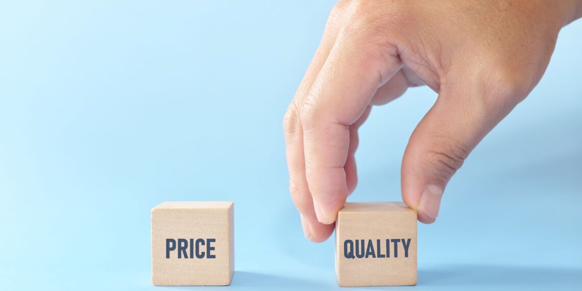 A hand is picking up a wooden block labeled "QUALITY" from a set of two blocks. The other block is labeled "PRICE." The blocks are set against a light blue background.