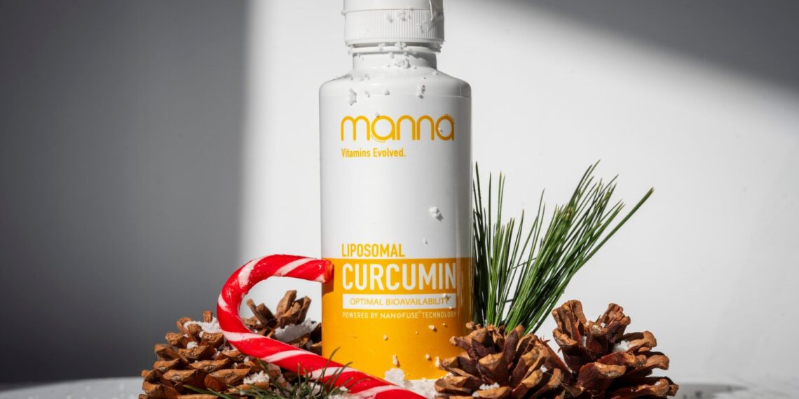 A bottle of Manna Liposomal Curcumin surrounded by pine cones, pine sprigs, snow, and a red and white candy cane, set against a white background.