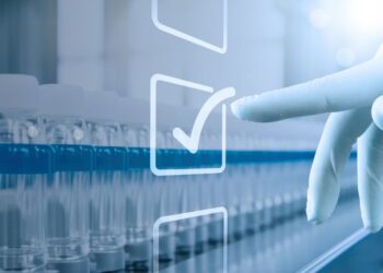 A gloved hand touches a virtual checkmark over a row of laboratory vials, indicating approval or selection.