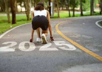 A person in athletic attire is crouched in a starting position on a path with "2025" painted on it, surrounded by trees.