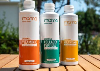 Three bottles of liposomal supplements on a wooden table: Vitamin C (orange), Collagen Peptides (green), and Multivitamin (yellow). Trees and buildings are blurred in the background.
