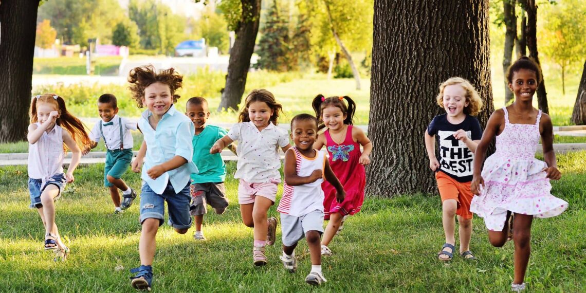 A group of children happily running on green grass in a park, with trees and a distant background.