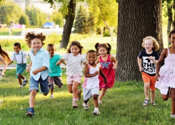 A group of children happily running on green grass in a park, with trees and a distant background.