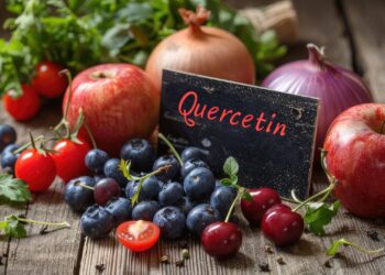 A group of apples, blueberries, cherries, tomatoes, onions, and herbs surround a card labeled "Quercetin" on a wooden surface.